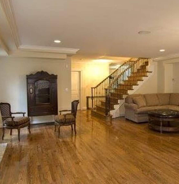 A basement room with wood flooring and a staircase leading upstairs