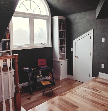 An attic room with wood flooring leading down to a small desk